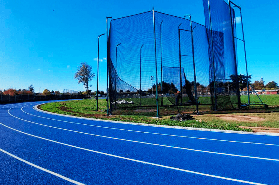 The bend of the Temuco track with a netted throwing cage standing on the grass infield behind it.