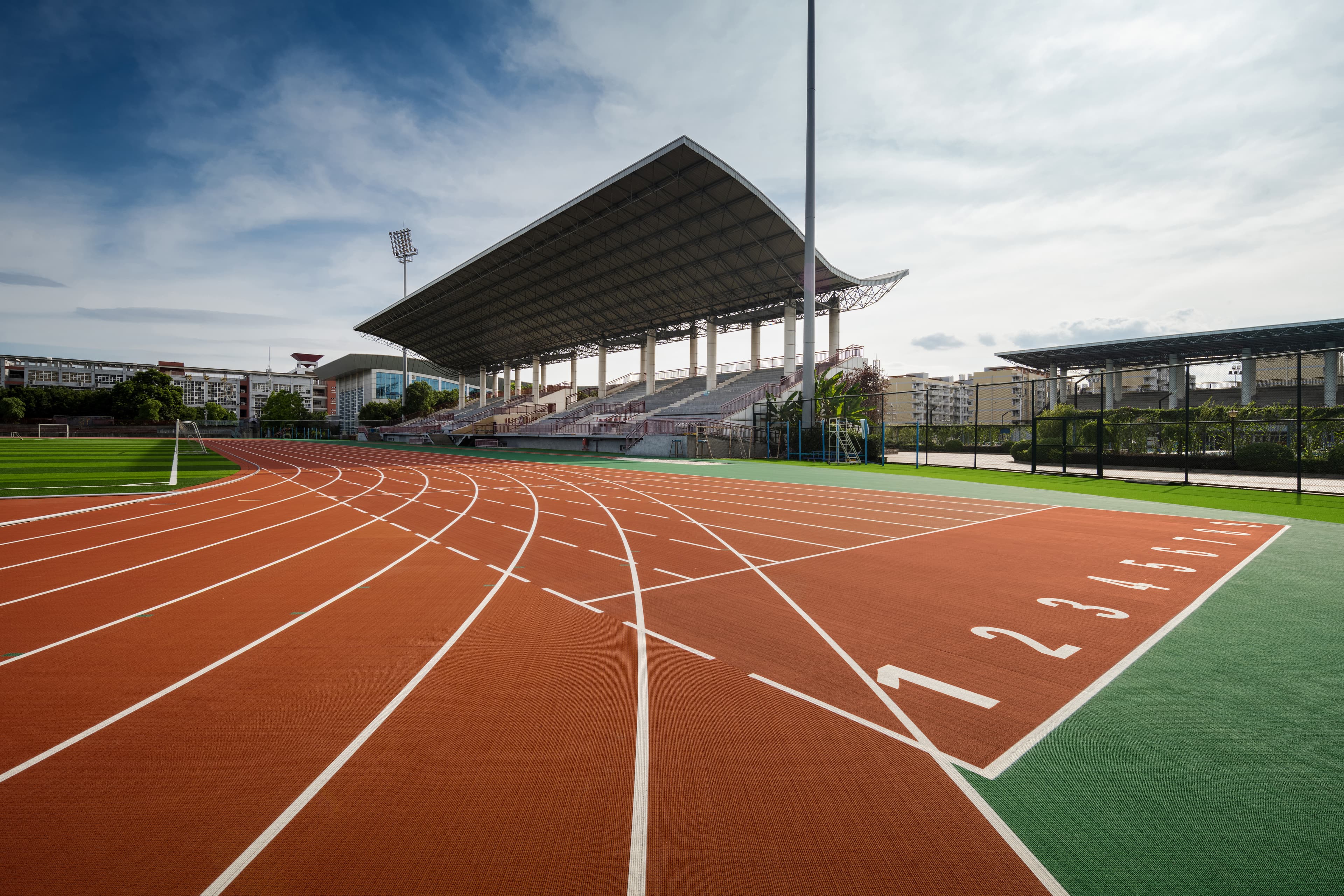 The eight-lane track at Beiyuan stadium seen from the start line, lanes numbered one to eight in white on the red surface, with the covered grandstand and floodlights behind.